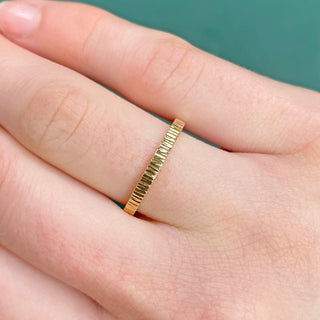 A slim 18ct gold wedding ring with a hammered tree bark texture, displayed on a finger