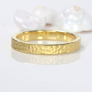 3mm wide 18ct gold wedding band with a flat profile and hammered finish, on a reflective surface