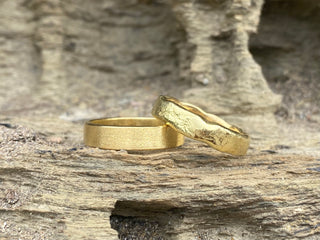 Two Ethical handmade 18ct gold wedding rings by Lilia Nash on rocky background.