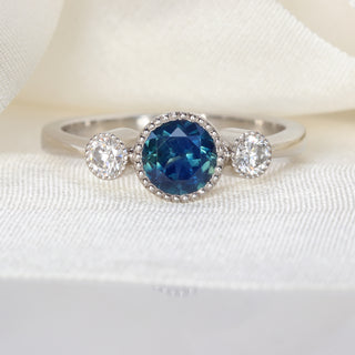 Natural unheated Parti sapphire trilogy engagement ring in platinum photographed on pale fabric.