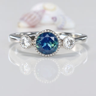 Close-up of platinum Parti sapphire and diamond trilogy ring on reflective background.