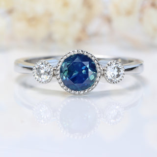 Handmade Parti sapphire and diamond trilogy ring in platinum on white background and faded floral backdrop.