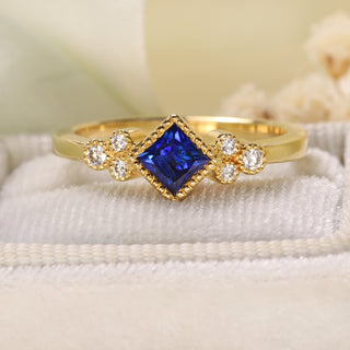 18ct gold handmade Blue sapphire and trilogy engagement ring by Lilia Nash on soft fabric.