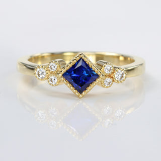 Handmade 18ct gold princess cut sapphire and diamond cluster ring with milgrain detail.