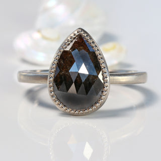Pear cut black diamond solitaire ring made from 18ct white gold, on a reflective surface