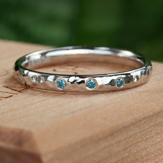 Platinum hammered wedding band with trio of blue diamonds, handmade ethical design.