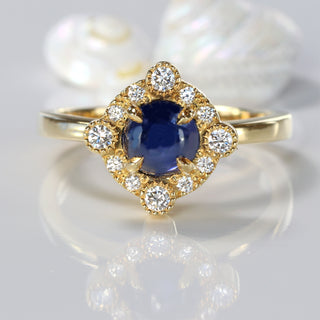 18ct gold blue sapphire cabochon ring with a diamond halo on reflective surface