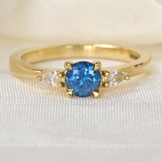 Handmade 18ct gold royal blue sapphire trilogy ring photographed on pale textured fabric.