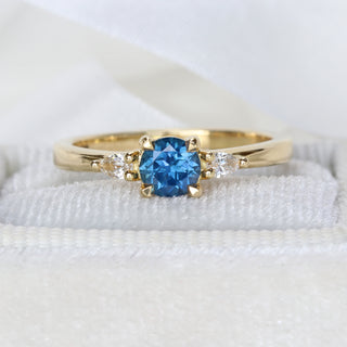 Handmade 18ct gold royal blue sapphire trilogy ring photographed on pale textured fabric.