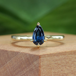 Deep blue teardrop sapphire engagement ring in 18ct gold presented on a wooden ring box.