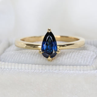 Pear cut sapphire engagement ring in 18ct gold photographed on cream fabric.