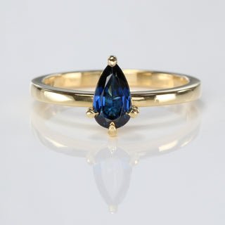 Handmade 18ct gold pear cut deep blue sapphire engagement ring on ivory background.