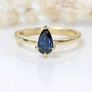 Angled view of pear cut blue sapphire engagement ring in 18ct gold