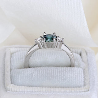 Side view of platinum teal sapphire trilogy engagement ring in a white ring box.