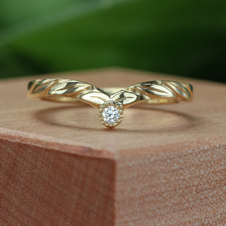 A 18ct gold wishbone style wedding ring with a central diamond accent and engraved leaf patterns on the band, displayed on a wooden block.
