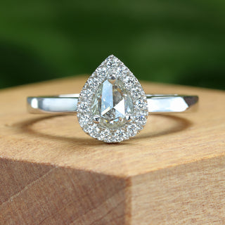 Pearl cut diamond halo engagement ring on wooden ring box.