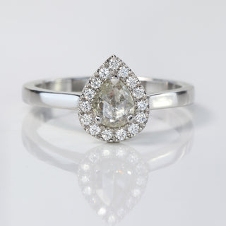 Handmade platinum pear diamond halo engagement ring with pavé setting on reflective surface.