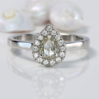 Handmade platinum pear diamond halo engagement ring with pavé setting on reflective surface.