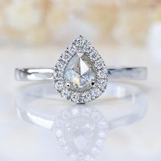 Front view of rose cut pear diamond halo ring photographed on pale floral background.