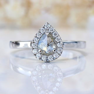 Front view of rose cut pear diamond halo ring photographed on pale floral background.