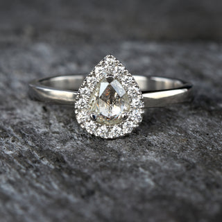 Platinum halo engagement ring with pear diamond photographed on dark textured background.