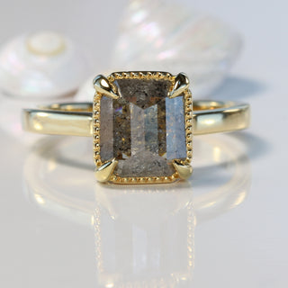 Emerald cut Salt and pepper diamond 18ct gold ring on reflective surface