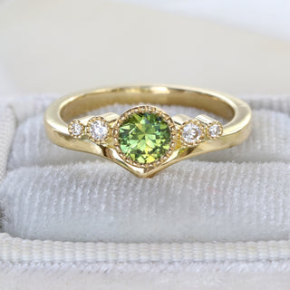 18ct gold wishbone engagement ring with green sapphire and diamonds photographed on pale fabric.