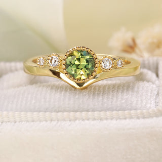 Handmade 18ct gold wishbone engagement ring with green sapphire photographed with green fabric background.