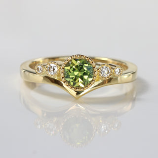 Handmade 18ct gold wishbone engagement ring with green sapphire and Canadian diamonds on reflective surface.