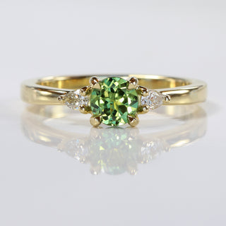 Green sapphire engagement ring in trilogy style, handmade  with fair trade sapphire and Canadian diamonds, on reflective grey background