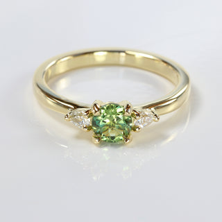 Top view of handmade trilogy engagement ring featuring a fair trade green sapphire and pear cut diamonds, on a grey background.