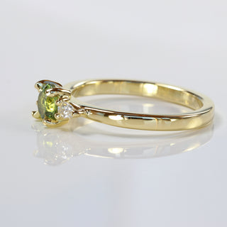 Side view of a hand-made sapphire and diamond trilogy engagement ring showing the 18ct gold band. Resting on a reflective background.