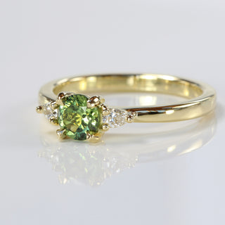 Angled view of a fair trade green sapphire and diamond trilogy engagement ring handmade from 18ct gold