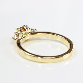 View of the back of the setting of a handmade trilogy engagement ring set with a fair trade green sapphire and pear cut diamonds, on a grey background.