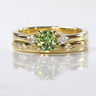 Wed-fit set of a handmade 18ct gold Green sapphire trilogy ring and bead set diamond wedding band, on a reflective grey backdrop.