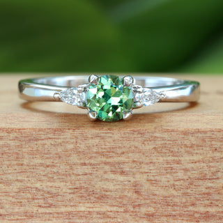 Green sapphire trilogy engagement ring in platinum photographed on Lilia Nash branded wooden box.