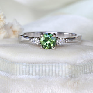 Handmade green sapphire trilogy engagement ring on felt box with white flowers.
