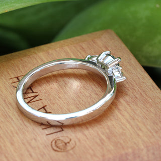 Handmade platinum green sapphire and diamond trilogy ring photographed against green foliage.