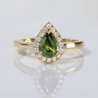 Handmade 18ct gold green sapphire halo engagement ring with Canadian diamonds on reflective surface.