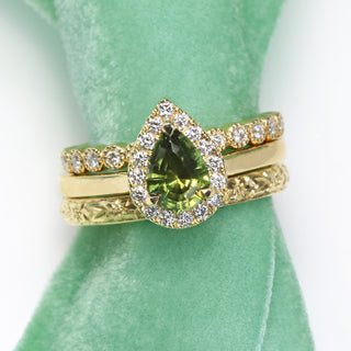 18ct gold green sapphire halo ring photographed on green fabric.