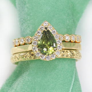 18ct gold green sapphire halo engagement ring paired with orange blossom engraved wedding ring and matching diamond eternity ring.