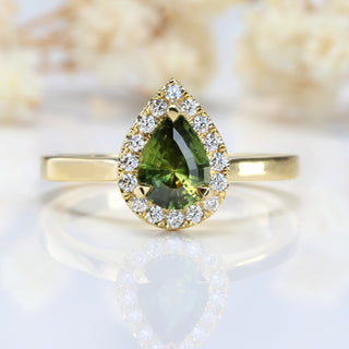Green sapphire engagement ring with a halo of diamonds, on a soft white floral backdrop.