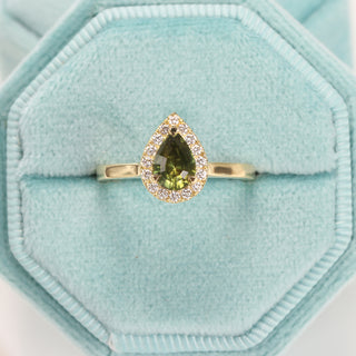 Pear cut green sapphire halo engagement ring in handmade 18ct gold displayed in a ring box.