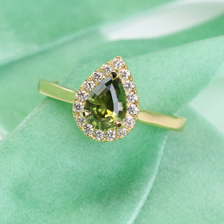 18ct gold green sapphire halo engagement ring photographed on green fabric at an angle.