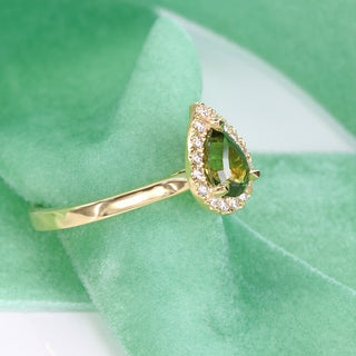 Pear cut green sapphire and diamond halo engagement ring shown at an angle on green fabric.