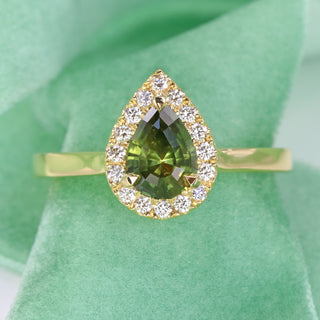 18ct gold green sapphire halo engagement ring photographed on green fabric.