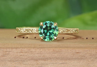 Handmade sustainable 18ct gold green sapphire solitaire engagement ring with hand engraved orange blossom and leaves pattern. Resting on a wooden box with green background