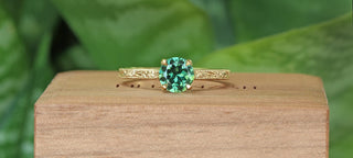 Banner of a 18ct gold green sapphire solitaire engagement ring with hand engraved floral detail