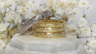 A stack of hand engraved 18ct gold wedding bands with floral patterns