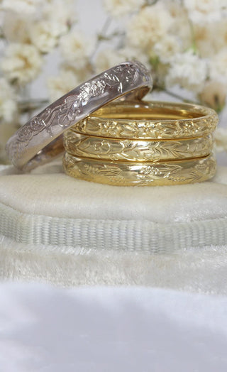 A stack of hand engraved 18ct gold wedding bands with floral patterns